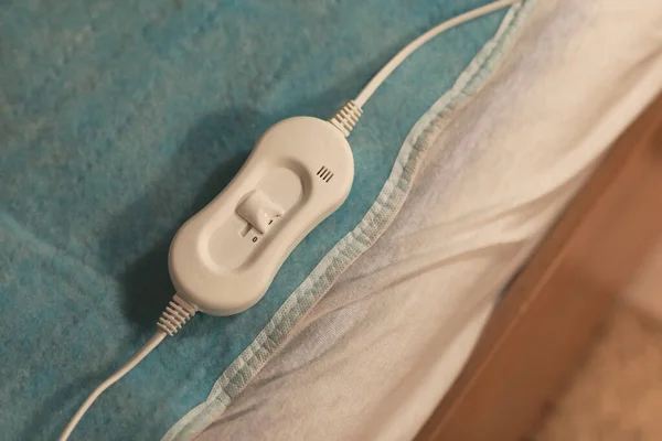 Electric heating pad with controller on bed at night, closeup