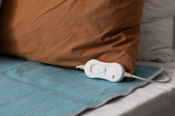 Electric heating pad with controller on bed in room, closeup