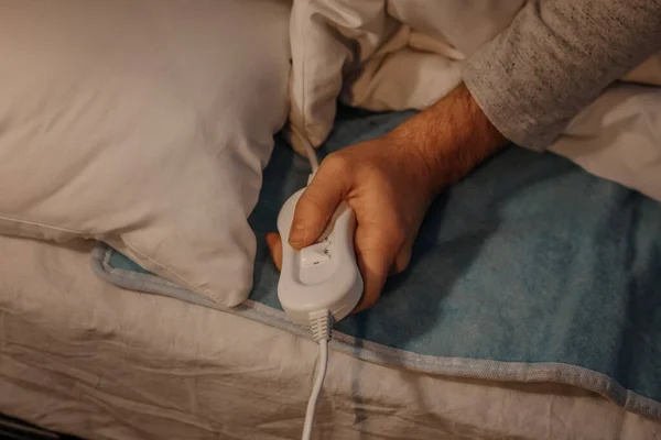 Young man turning on electric heating pad in bedroom at night, closeup