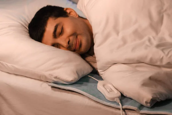 Young man sleeping on electric heating pad in bedroom at night