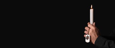 Yanan mum ve künyeli Yahudi bir adamın elleri. Soykırım kurbanlarını onurlandırıyor. Karanlık bir arkaplanda mesaj için yer var.