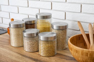 Cam kavanozlar ve farklı tahıllar. Hafif tuğla duvarın yanındaki ahşap masada.