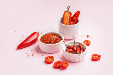 Bir kase chipotle chili flakes, pembe arka planda taze ve kurutulmuş jalapeno biberi.