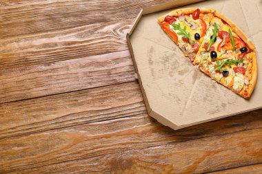 Tahta arka planda lezzetli pizza parçaları olan karton kutu.