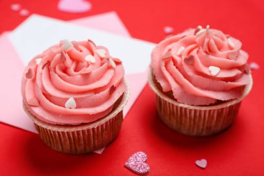 Kırmızı arkaplanda Sevgililer Günü için lezzetli kekler, kalpler ve zarf, yakın plan.