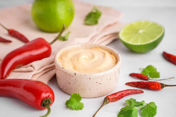 Bowl of tasty chipotle sauce and jalapeno peppers on light background