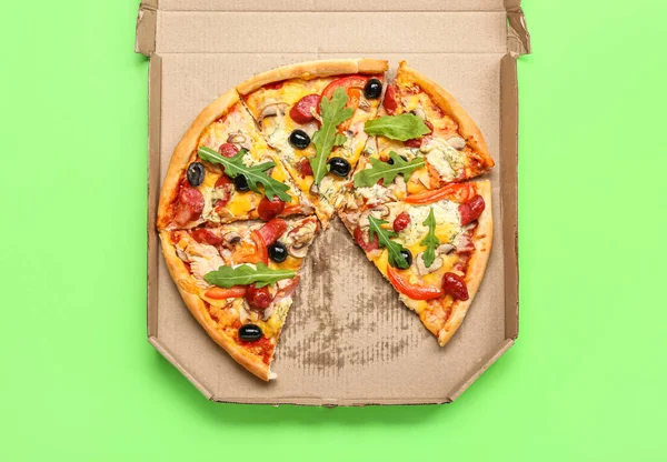 Cardboard box with delicious pizza on green background