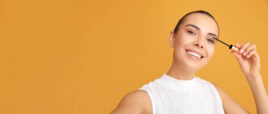 Güzel genç bir kadın turuncu arka plana rimel sürerken mesaj için yer açıyor.