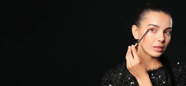 Güzel genç bir kadın karanlık arka plana rimel sürüyor ve yazı için boşluk var.