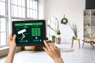 Bir kadının elleri ekranda akıllı ev güvenlik sistemi olan tablet bilgisayarı tutuyor.