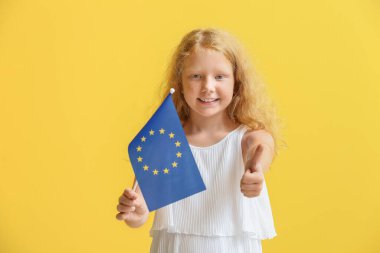 Avrupa Birliği bayrağı taşıyan küçük kız sarı arka planda baş parmak gösteriyor