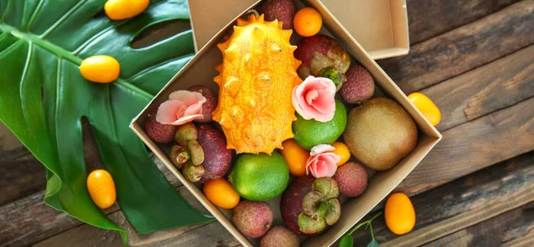 Box with assortment of tasty exotic fruits on wooden background, top view