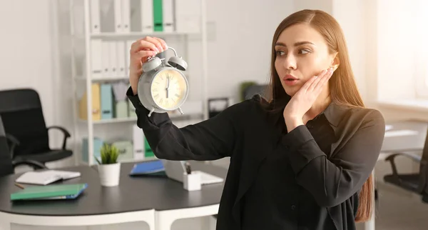 Troubled young woman with alarm clock in office. Time management concept