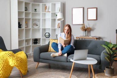 Evdeki siyah koltukta kitap okuyan güzel bir kadın.