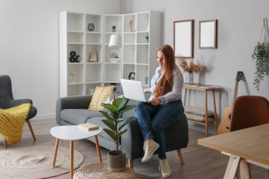 Evdeki siyah koltukta dizüstü bilgisayar kullanan güzel bir kadın.