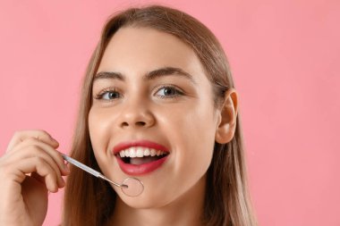 Pembe arka planda dişçi aletli genç kadın, yakın plan.