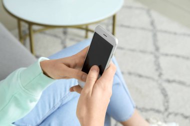 Evde akıllı telefon kullanan genç bir kadın, yakın plan.