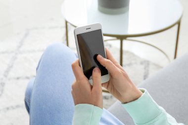 Evde akıllı telefon kullanan genç bir kadın, yakın plan.