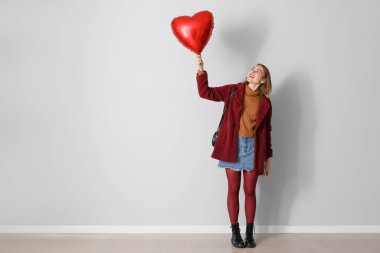 Gri duvarın yanında kalp şeklinde balonu olan genç bir kadın. Sevgililer Günü kutlaması