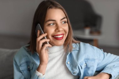 Evde akıllı telefonla konuşan genç bir kadın, yakın plan.