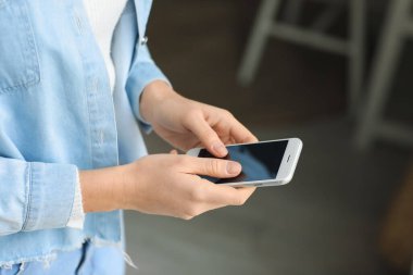 Evde akıllı telefon kullanan genç bir kadın, yakın plan.