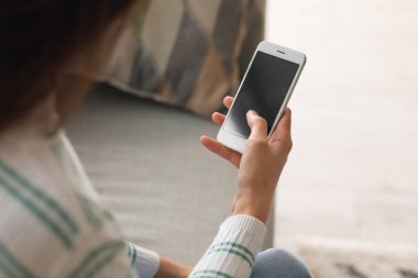 Evde akıllı telefon kullanan genç bir kadın, yakın plan.