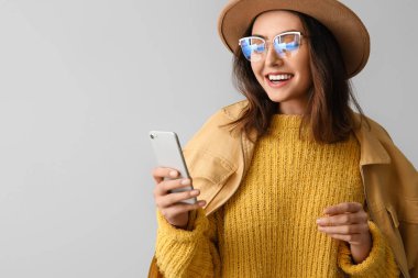 Gri arka planda cep telefonu kullanan şapkalı genç bir kadın.