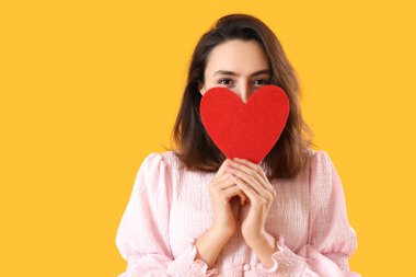 Sarı arka planda kağıt kalpli genç bir kadın. Sevgililer Günü kutlaması