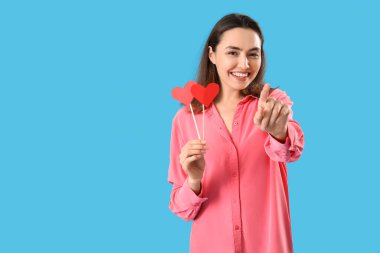 Mavi arka plandaki izleyiciye bakan kağıt kalpli genç bir kadın. Sevgililer Günü kutlaması