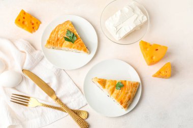 Lezzetli peynirli turta, maydanoz yaprağı, çatal bıçak takımı ve malzemelerle dolu tabaklar.