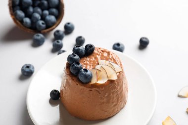 Lezzetli çikolatalı puding, hindistan cevizi dilimleri ve beyaz arka planda yabanmersini tabağı.