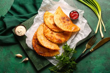 Lezzetli chebureks, maydanoz, soğan, sarımsak, sos ve çatal bıçak seti yeşil grunge arka planda.