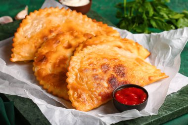 Parşömen tahtası, lezzetli cheburekler ve yeşil grunge arkaplanda sos