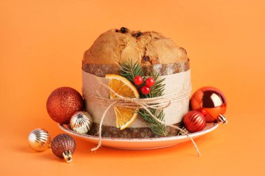 Lezzetli Panettone tabağı ve turuncu arka planda Noel dekoru.