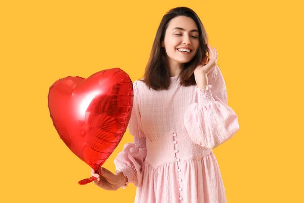Young woman with heart shaped balloon on yellow background. Valentine\'s Day celebration