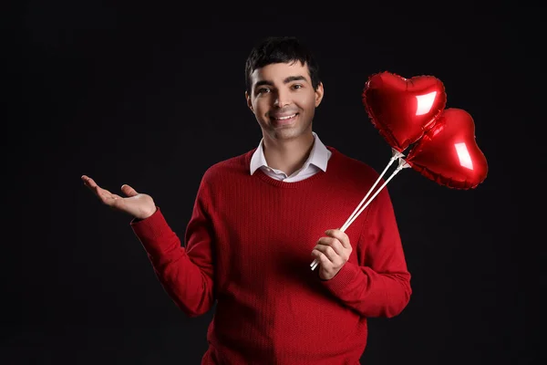 Young man with heart-shaped balloons on black background. Valentine\'s Day celebration