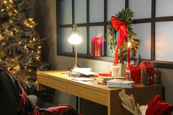 Modern workplace with glowing lamp and Christmas wreath hanging on window in dark office