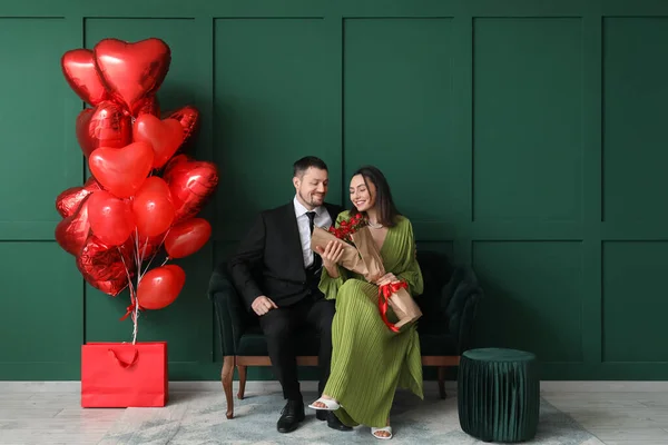 Happy couple in love with roses sitting on sofa near green wall. Valentine\'s Day celebration
