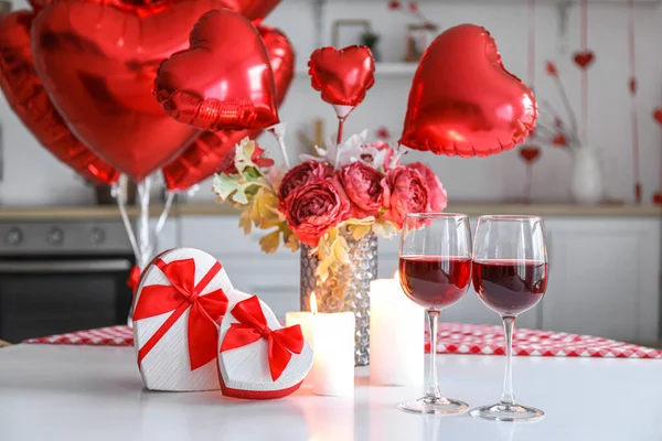 Dining table with gifts, glasses of wine, candles, flowers and balloons for Valentine\'s Day in kitchen