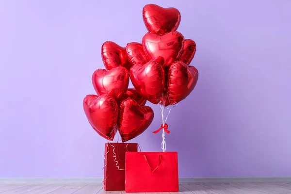Shopping bags with heart-shaped balloons for Valentine\'s Day near lilac wall