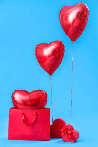 Shopping bag with heart-shaped balloons and gifts for Valentine\'s Day on blue background