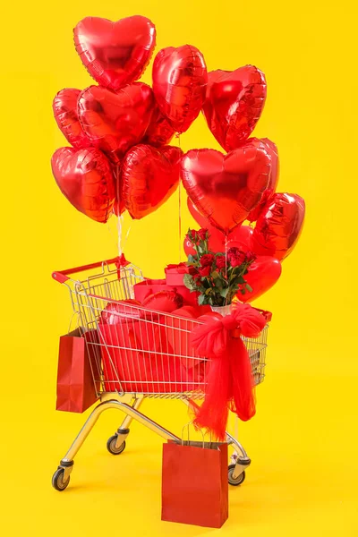 Shopping cart with gifts, roses and balloons for Valentine\'s Day on yellow background