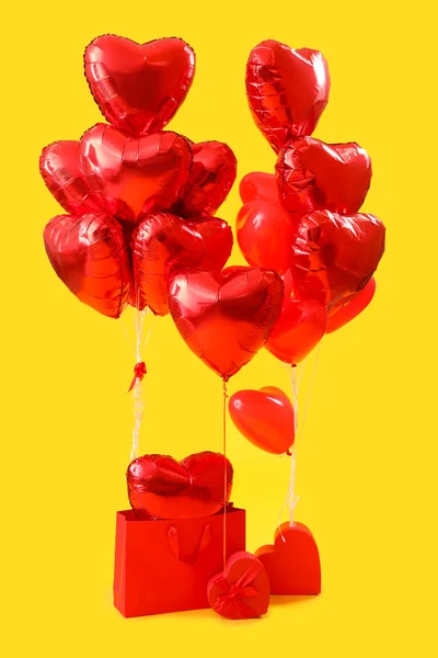 Shopping bag with heart-shaped balloons for Valentine\'s Day on yellow background