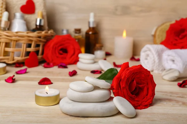Spa stones with rose and candle on wooden table, closeup. Valentine\'s Day celebration