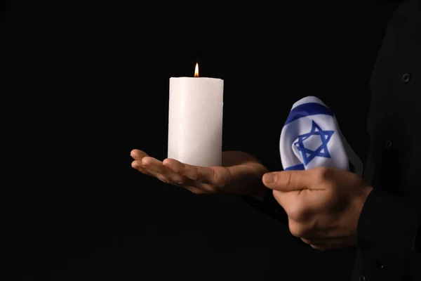 Jewish man with candle and flag of Israel on dark background, closeup. International Holocaust Remembrance Day