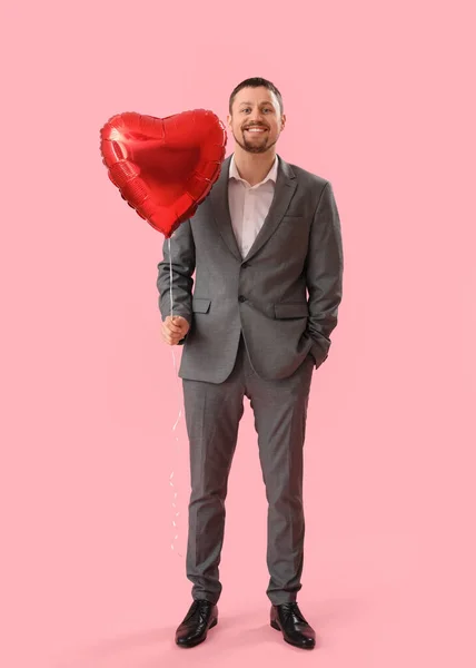 Handsome man with heart-shaped balloon on pink background. Valentine\'s Day celebration