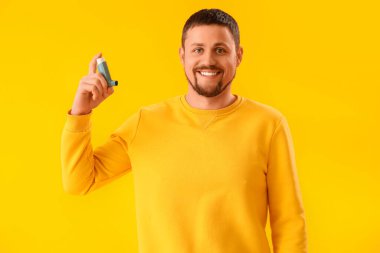 Sarı arka planda astım spreyi olan adam.