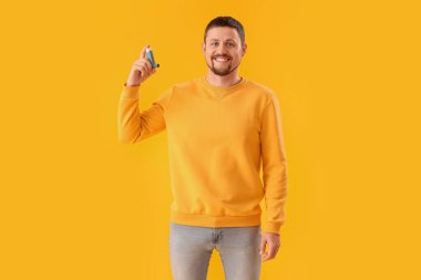 Sarı arka planda astım spreyi olan adam.