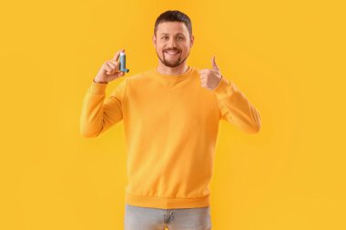 Astım spreyli adam sarı arkaplanda baş parmağını gösteriyor.