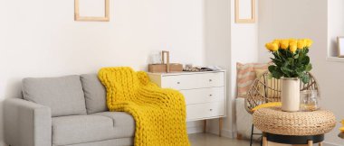 İçinde güzel sarı güller ve odanın içinde gri bir kanepe olan vazo.